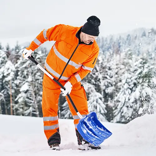 Kommunaler Service Arbeiter in oranger Sicherheitsuniform reinigt Wege und Straßen nach Schneefall